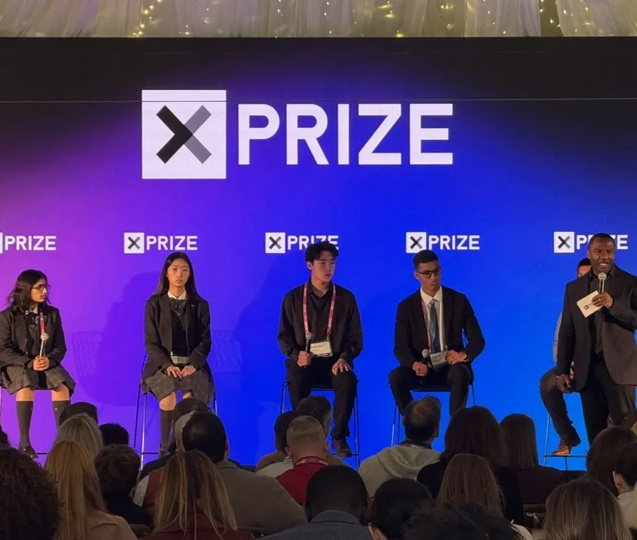 Four students seated on stage at an XPRIZE event while a moderator speaks to the audience
